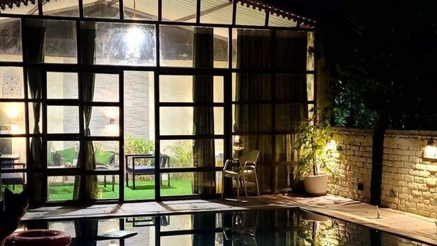 A pool area with a glass enclosure, a chair, and a potted plant.