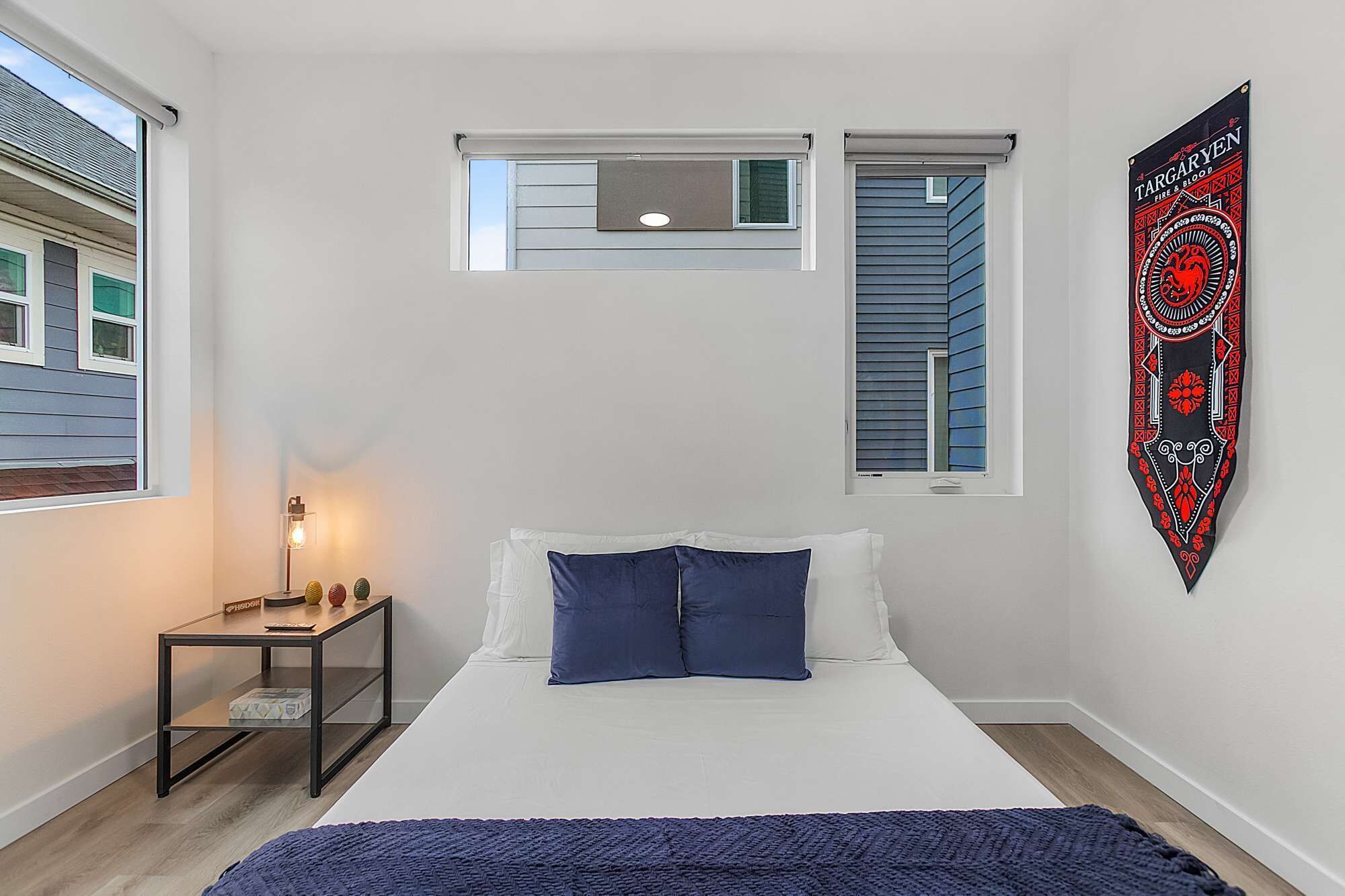 A bedroom with a bed, a nightstand, a lamp, a window, and a wall hanging.