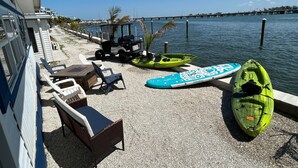 Una propietat al costat del mar amb zona de terrassa que inclou mobiliari exterior, kayaks i un vehicle elèctric de golf.