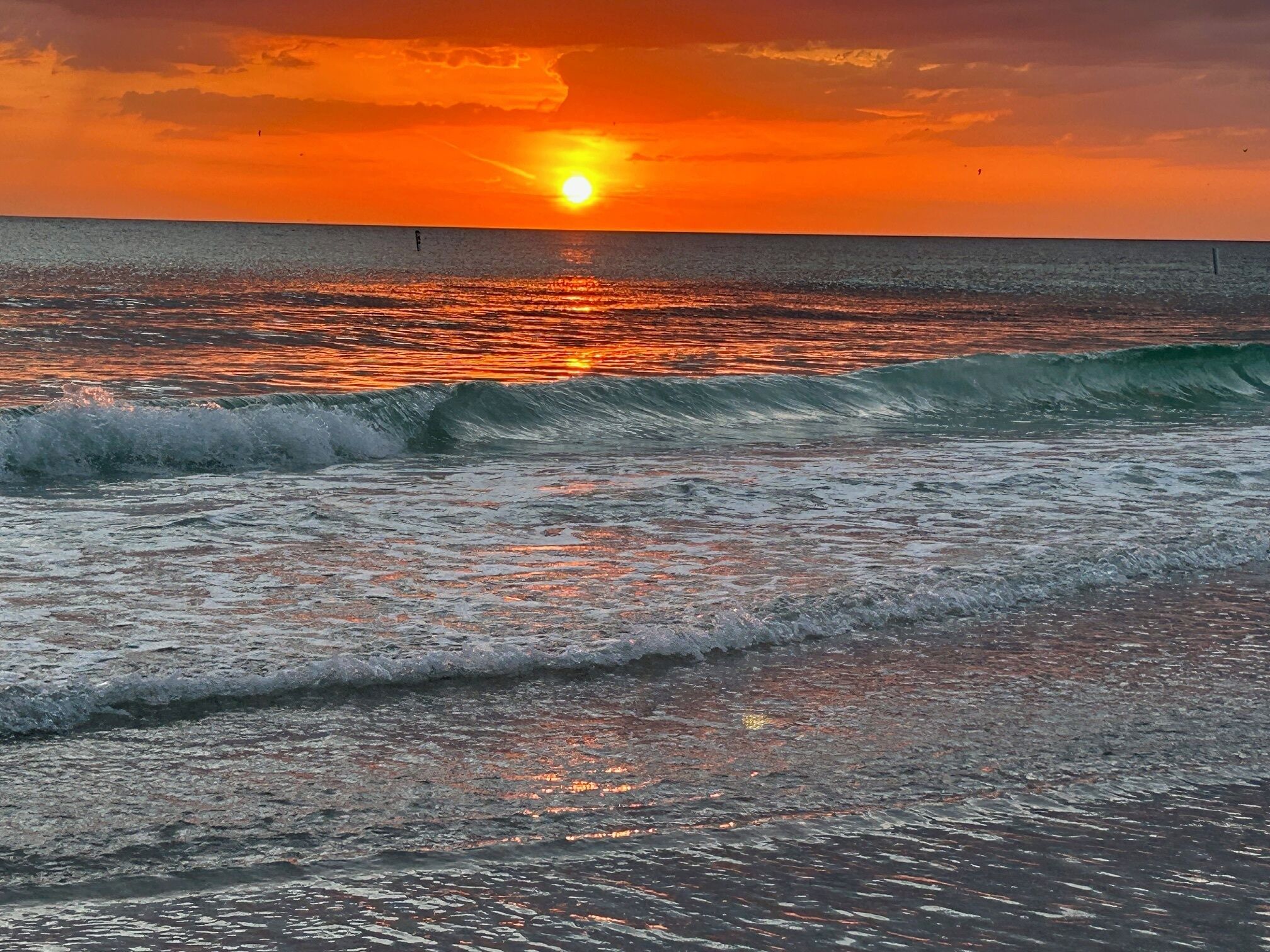 A sunset over the ocean with waves approaching the shore.