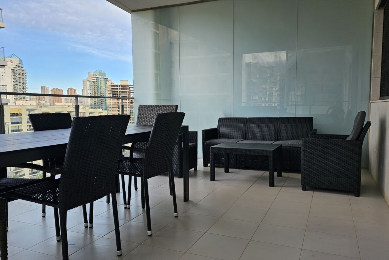A balcony with a dining table and chairs, a sofa, and a view of a cityscape.