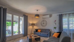 Un salon comprenant un canapé, une table basse, un lampadaire, une horloge murale et une fenêtre avec des rideaux.
