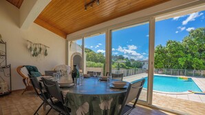 Un coin repas avec une table dressée pour quatre personnes, de grandes fenêtres et une piscine à l’extérieur.