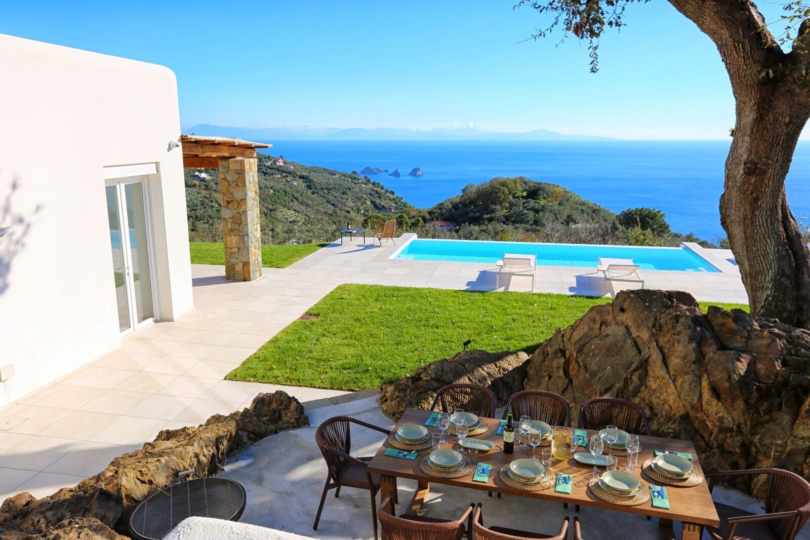 Ein Essbereich mit Blick auf das Meer, einen Pool und eine gebirgige Landschaft.