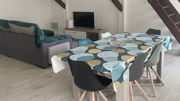 A modern living room with a dining area, featuring a staircase, a sofa, a TV, and a table with chairs. - Bel et Spacieux Appartement (Rives)