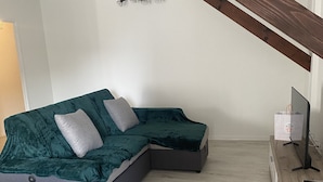 A modern living room with a sectional sofa, a wooden TV stand, and a ceiling with exposed beams. - Bel et Spacieux Appartement (Rives)