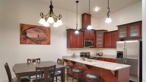 A modern kitchen with wooden cabinets, a stainless steel refrigerator, a granite countertop, and a dining area with a table and chairs.