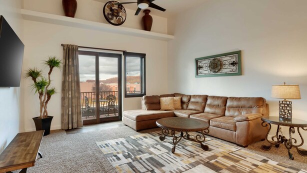 A living room with a leather sofa, a coffee table, a TV, and a balcony with a view.