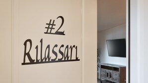 Een kamer met een bordje waarop staat '#2 Rilassati' en een aan de muur bevestigde televisie.