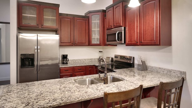 Una cocina con encimeras de granito, electrodomésticos de acero inoxidable, armarios de madera e iluminación colgante.