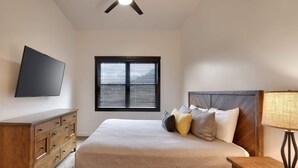 Un dormitorio con cama, cómoda de madera, televisión, ventana y ventilador de techo.