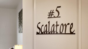 Eine Wand mit einem Schild, auf dem '#5 Scalatore' steht, in einem Raum mit einer Couch und einer Lampe.