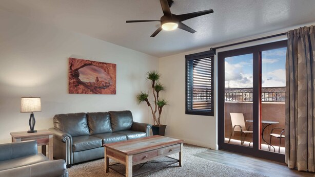 A living room with a leather sofa, a wooden coffee table, a floor lamp, a potted plant, and a painting on the wall.