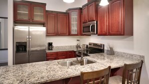 A kitchen with granite countertops, stainless steel appliances, wooden cabinets, and pendant lighting.
