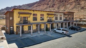 A two-story building with a yellow facade, multiple balconies, and a parking lot.