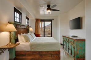 A bedroom with a bed, a ceiling fan, a TV, and a view of the outdoors.