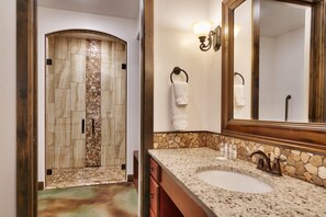 Une salle de bain dotée d’une douche à mosaïque de pierre, d’un lavabo avec un plan de travail en pierre et d’un miroir avec un cadre en bois.