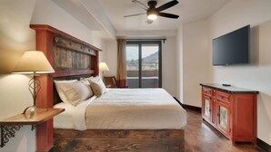 A bedroom with a bed, a ceiling fan, a TV, a wooden cabinet, and a view of the outdoors. - Luxury Downtown Rental (Hot Tub/Pet Friendly) #9 (Moab)