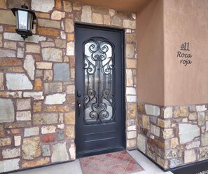 A stone wall entrance with a black door featuring decorative ironwork.