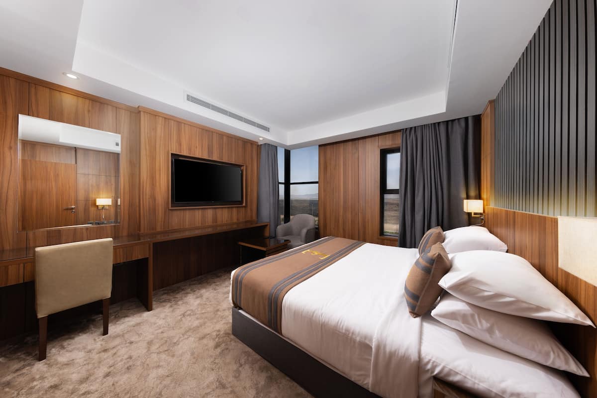 Une chambre d’hôtel avec un grand lit, un bureau, une chaise, une télévision et une vue sur l’extérieur.