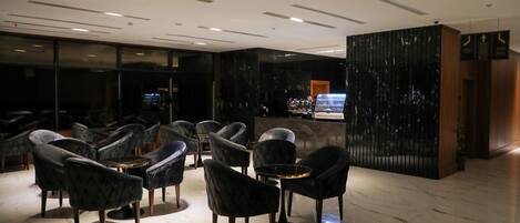 Un hall d’entrée moderne avec des fauteuils noirs à revêtement en tissu, un comptoir d’accueil et un sol en marbre.