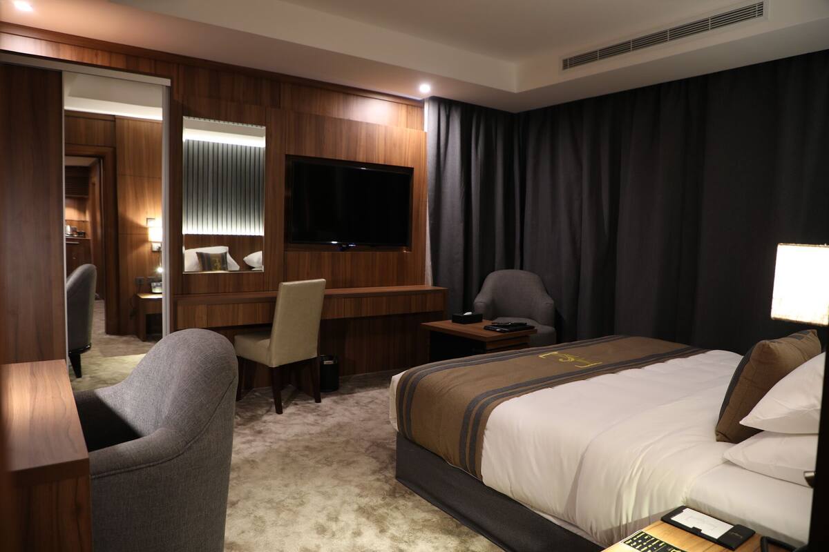 Une chambre d’hôtel avec un grand lit, un bureau avec une chaise, une télévision et une petite table avec une lampe.