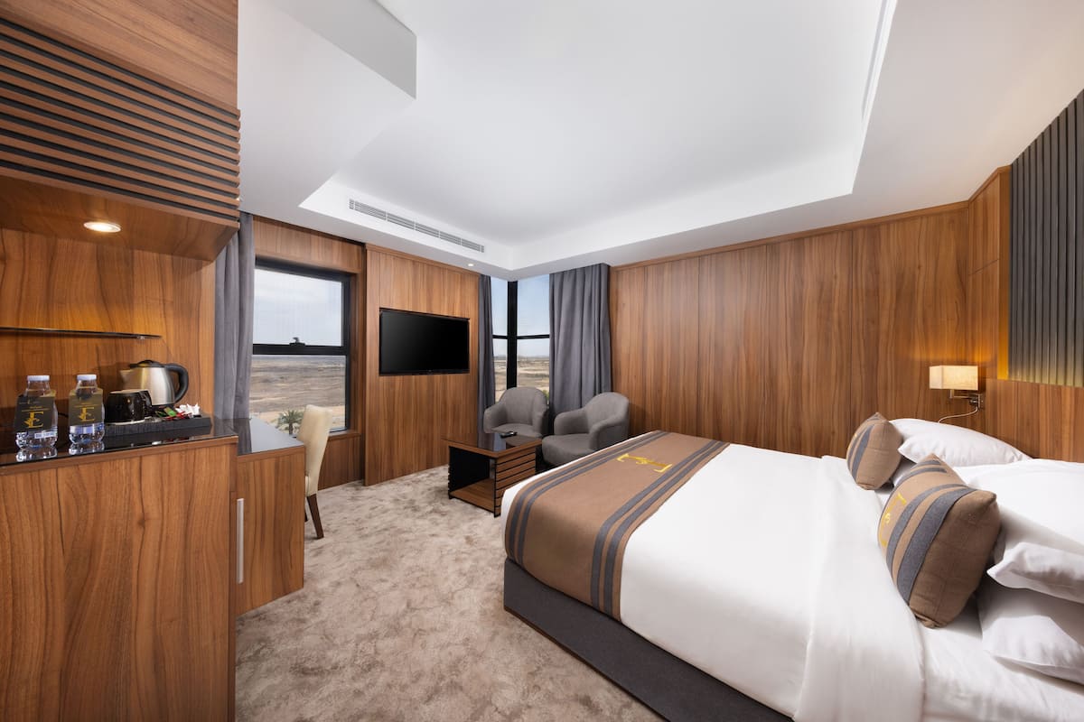 Une chambre d’hôtel avec un grand lit, un bureau doté d’un téléviseur à écran plat, une chaise et une vue sur le désert par la fenêtre.