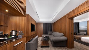 A modern hotel room with a wooden interior, a sofa, a coffee table, a TV, and a bed. - E hotel (Madinah)