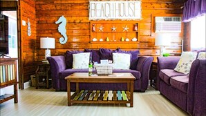 A cozy room with wooden walls, a seahorse decoration, and a 'BEACHHOUSE' sign. There are purple sofas with pillows, a wooden coffee table, and a small side table with a lamp. - Sea Bright Beach House Sleeps 6 Perfect for a Family with little ones! (Sea Bright)