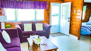 A cozy cabin interior with a purple sofa set, a wooden coffee table, and a door leading to a bedroom. - Sea Bright Beach House Sleeps 6 Perfect for a Family with little ones! (Sea Bright)