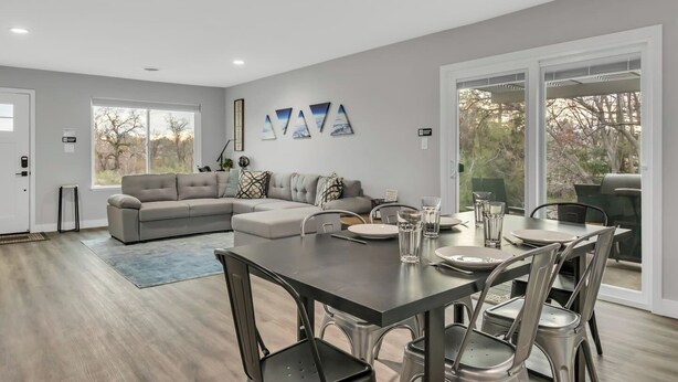 A modern living room with a sectional sofa, a dining table with chairs, and a large sliding glass door leading to an outdoor area.