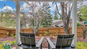 A covered patio with two chairs and a table, surrounded by a wooden fence and trees.