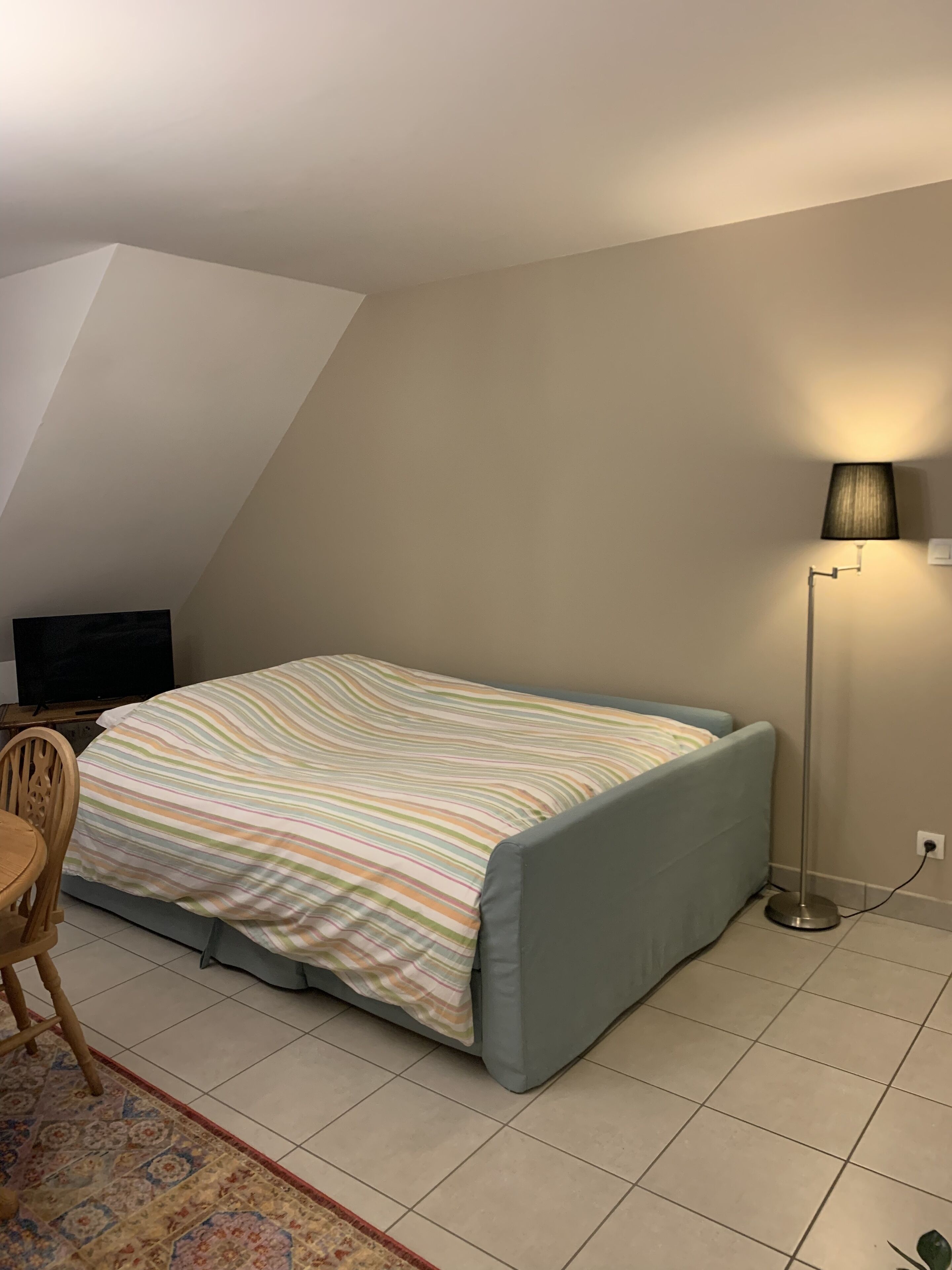 Quarto com cama, escrivaninha, cadeira, abajur e televisão.