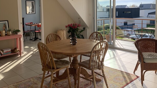Un coin repas avec une table et des chaises en bois, un lustre et une vue sur l’extérieur.