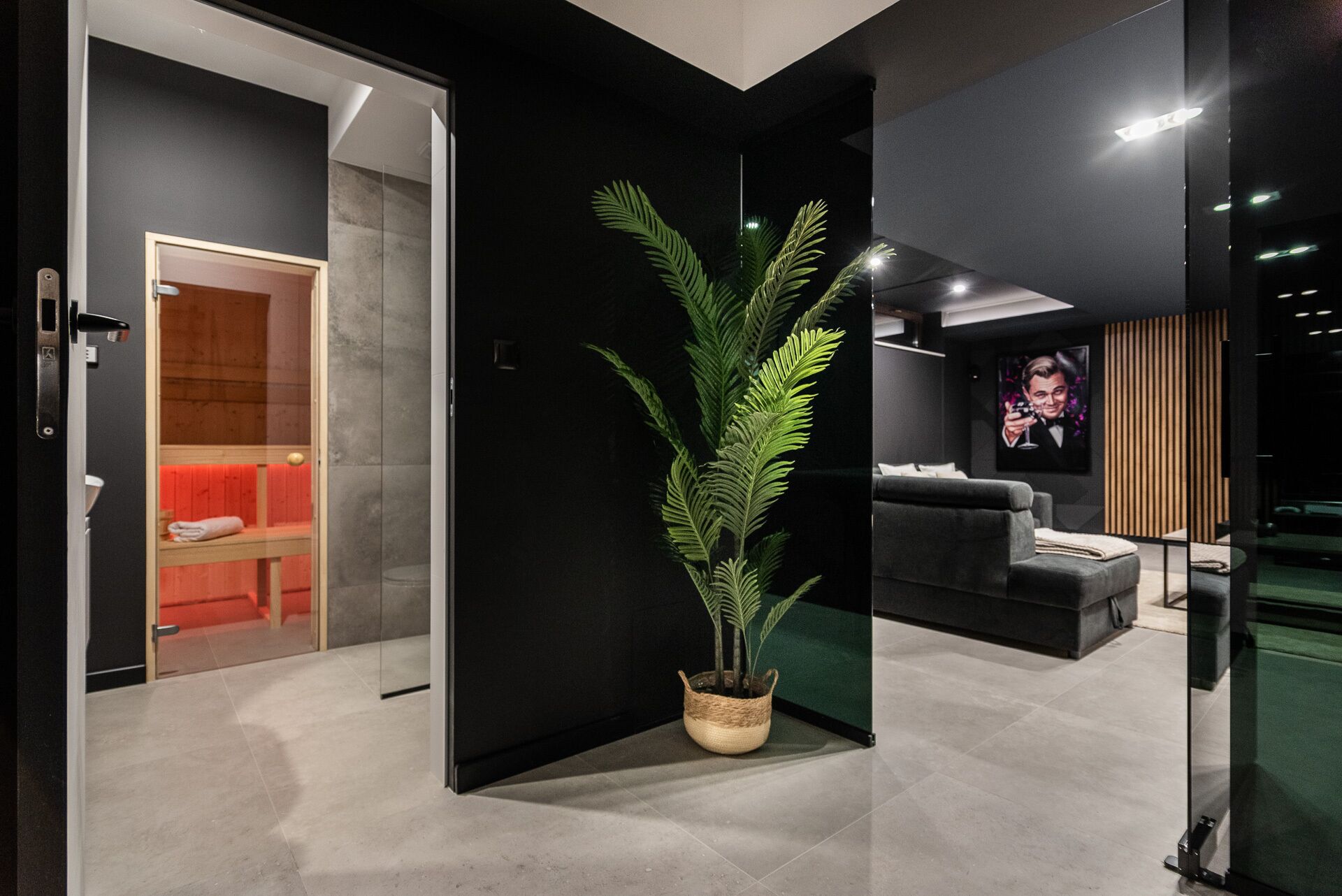 Un intérieur moderne avec une cloison en verre, un coin salon avec un canapé, un téléviseur et une plante en pot.
