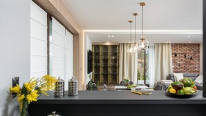 A modern kitchen with a black countertop, a dining area with a brick wall, and a living room with a grey sofa.