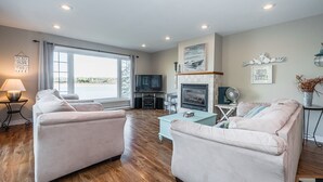 A modern living room with two sofas, a TV, a fireplace, and large windows offering a view of the outdoors. - Starlight Shores - Serene Lakefront Retreat: Explore and Unwind (Miller Lake)