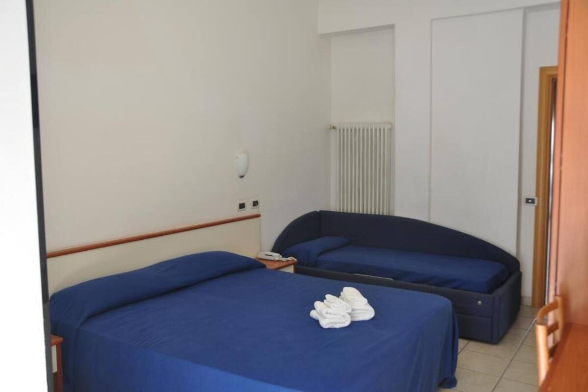 Habitación de hotel con dos camas, un radiador, un teléfono y una puerta de madera.