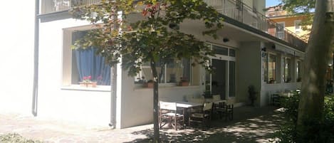 A building with a balcony, outdoor seating area, and a tree.