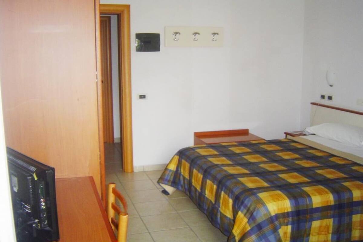 Un dormitorio con una cama, una mesita de noche de madera, una silla y un televisor.