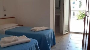A hotel room with two beds, each with a blue bedspread and white pillows. There is a sliding glass door leading to a balcony.