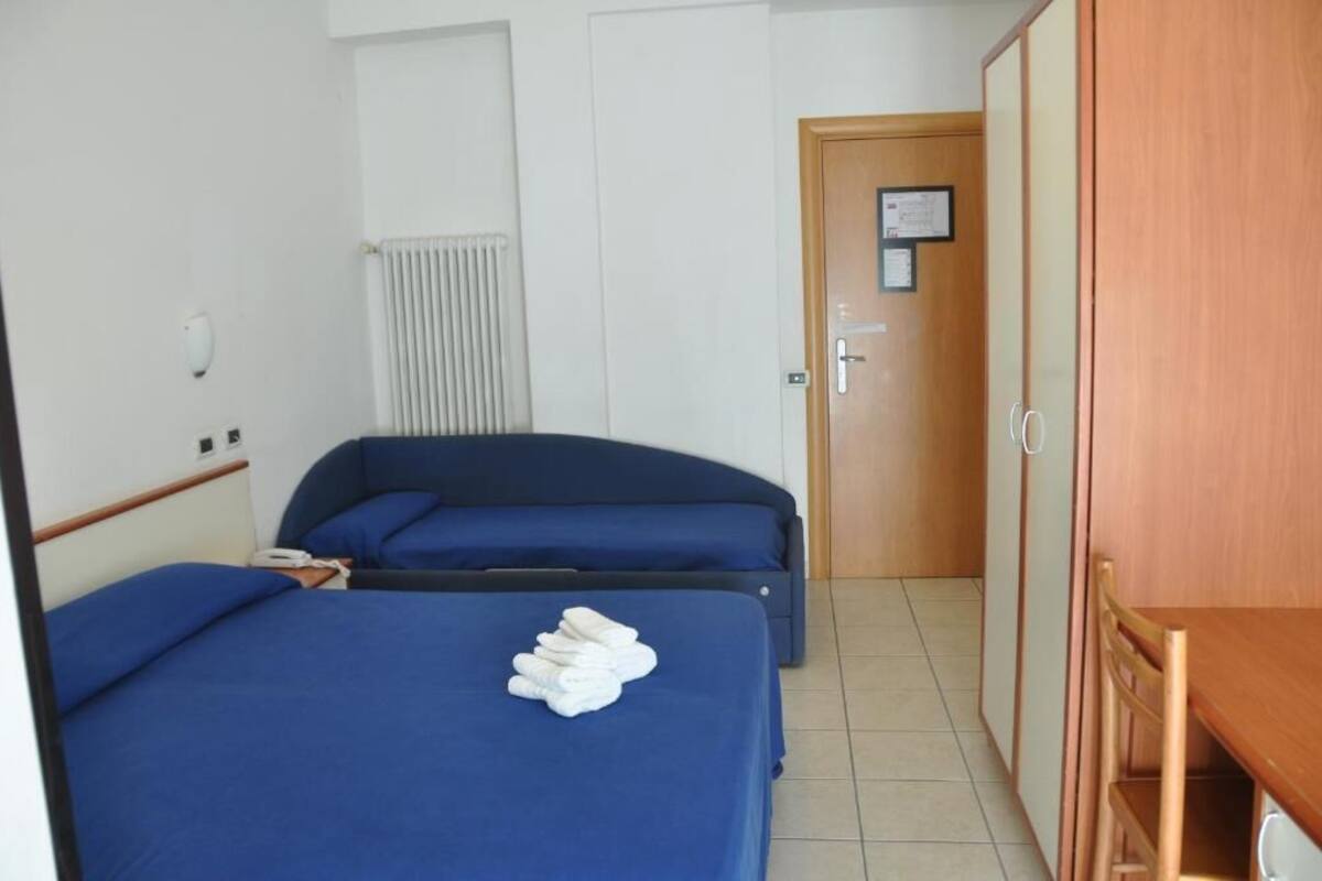 Habitación con dos camas, un armario de madera, un radiador y una puerta con un aviso.