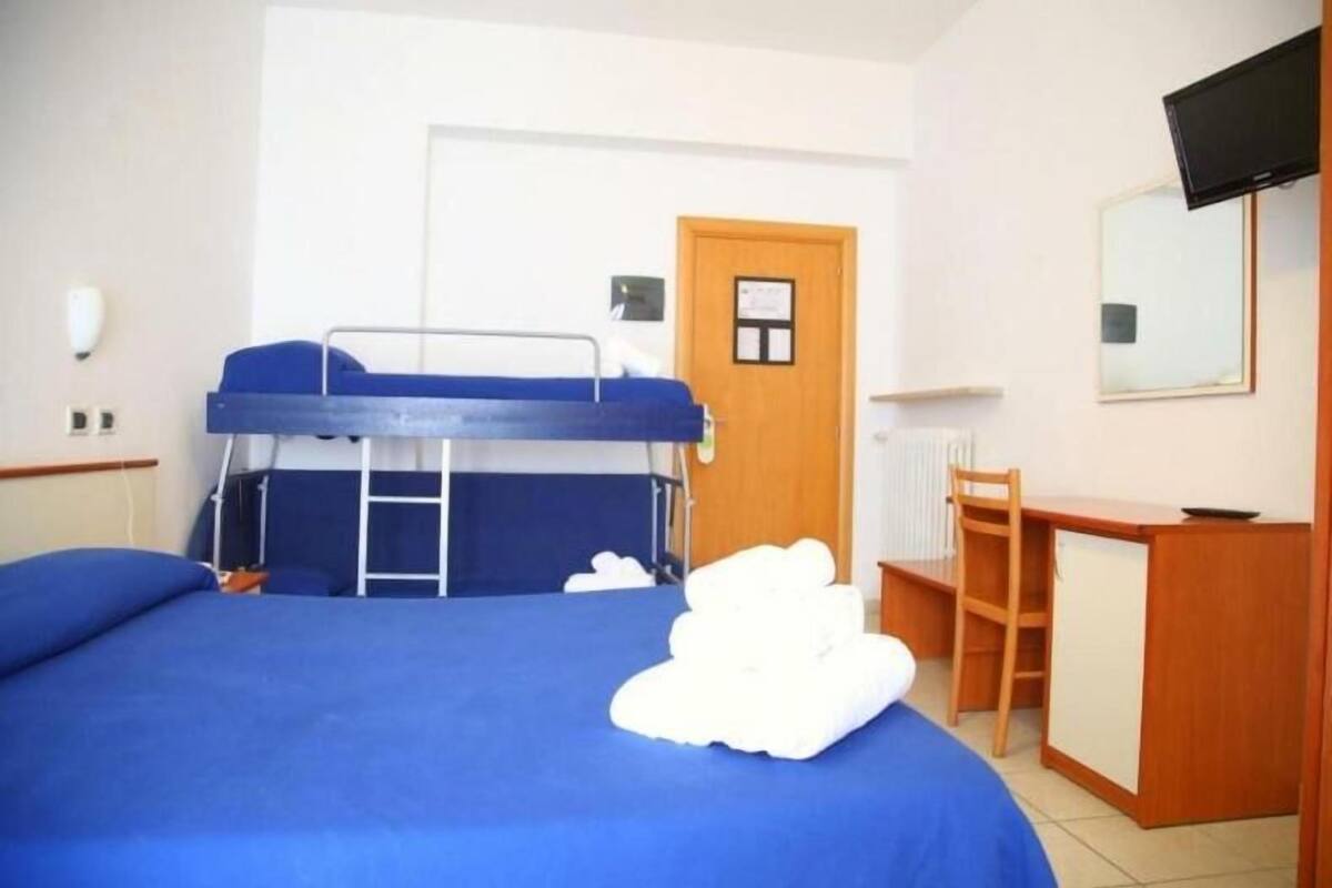 Una habitación de hotel con literas, un escritorio, una silla, un televisor y una puerta.