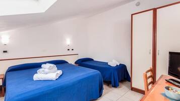 Ein Hotelzimmer mit zwei Betten, jedes mit einer blauen Bettdecke und weißen Handtüchern ausgestattet. Ein Holztisch steht dort mit einer Schüssel und einer Fernbedienung darauf.
