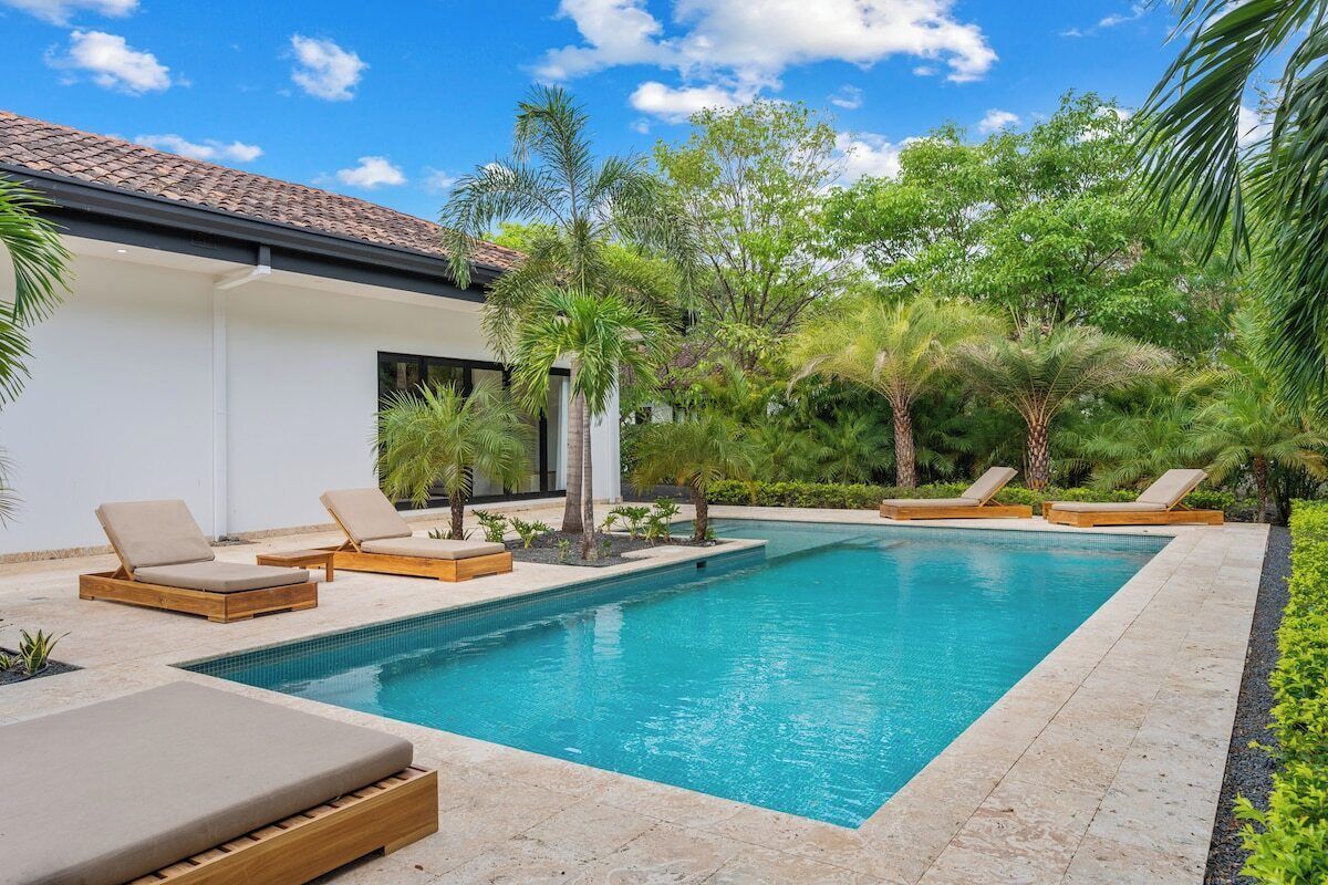 Una piscina con sillas de descanso, rodeada de plantas tropicales y un edificio con tejado de baldosas.