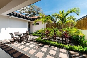 An outdoor patio with a table and chairs, surrounded by a garden with various plants and a wooden fence. - Villa OSU (Reserva de Golf, Hacienda Pinilla)