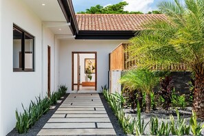 A modern house with a tiled roof, a stone pathway leading to the entrance, and tropical plants. - Villa OSU (Reserva de Golf, Hacienda Pinilla)