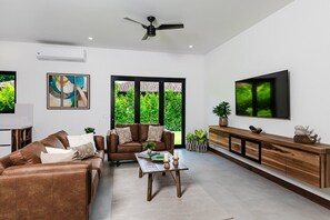 A modern living room with a brown leather sofa, a wooden coffee table, and a TV mounted on the wall. - Villa OSU (Reserva de Golf, Hacienda Pinilla)