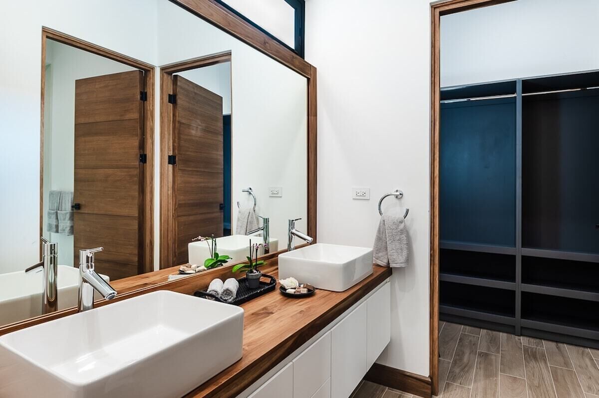 A modern bathroom with two sinks, a large mirror, and a wooden vanity.