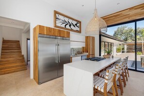 A modern kitchen with a large island, stainless steel appliances, and a dining area with wooden chairs.